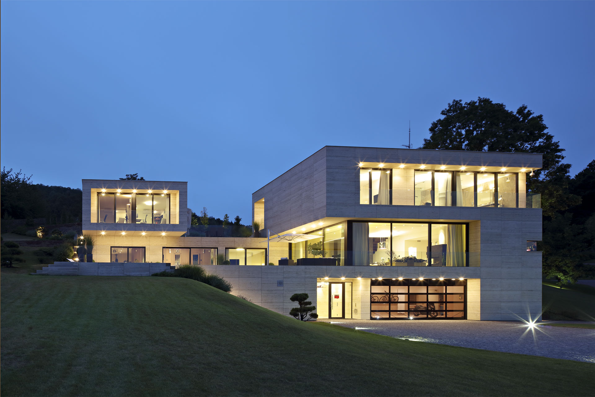 Wohnhaus bei Nacht mit beleuchteter Haustür und großen Fensterflächen